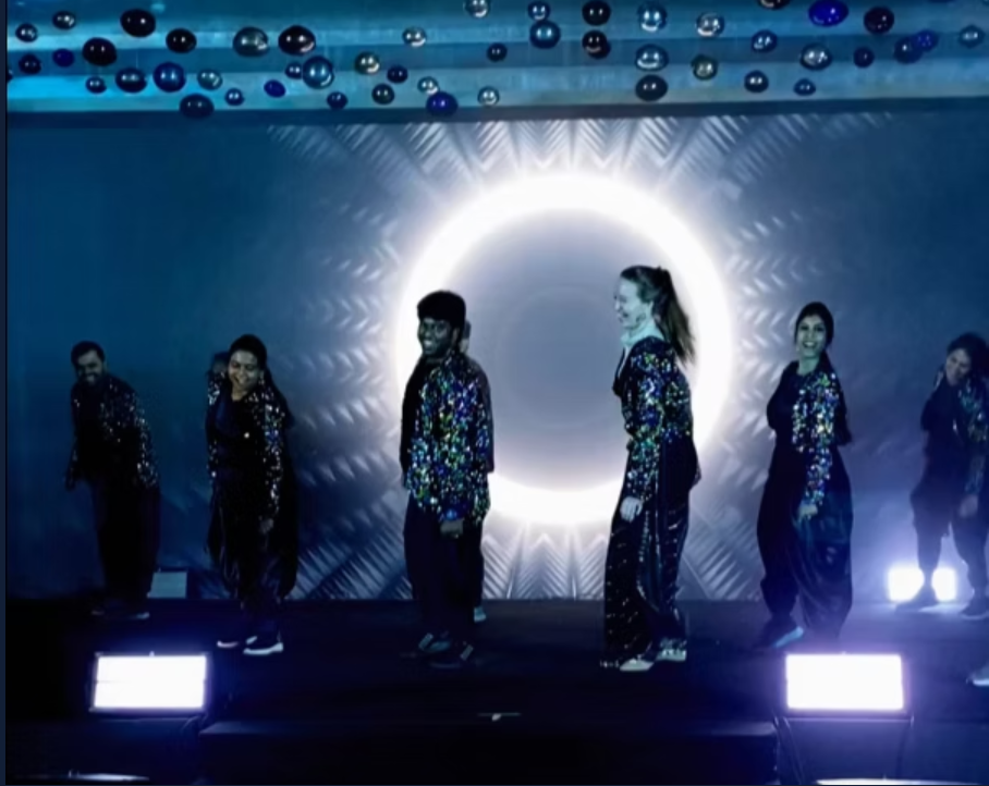 Dance troupe performing on a dark stage with a light ring
